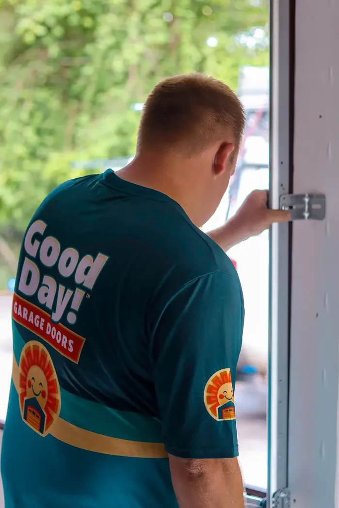 Good Day Garage Doors technician from behind reaching toward side track hardware on a white sectional garage door opening.