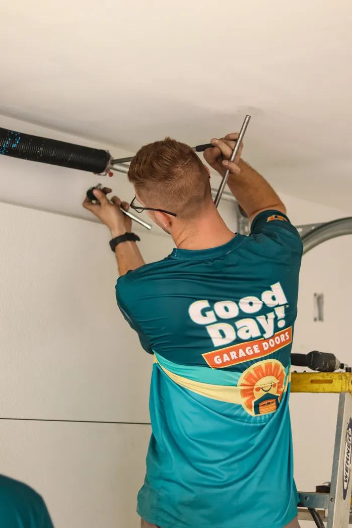 Good Day Garage Doors technician using winding bars to adjust a garage door torsion spring at the header.